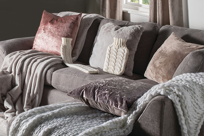 Cosy living room with a grey sofa covered in velvet and furry cushions and throws