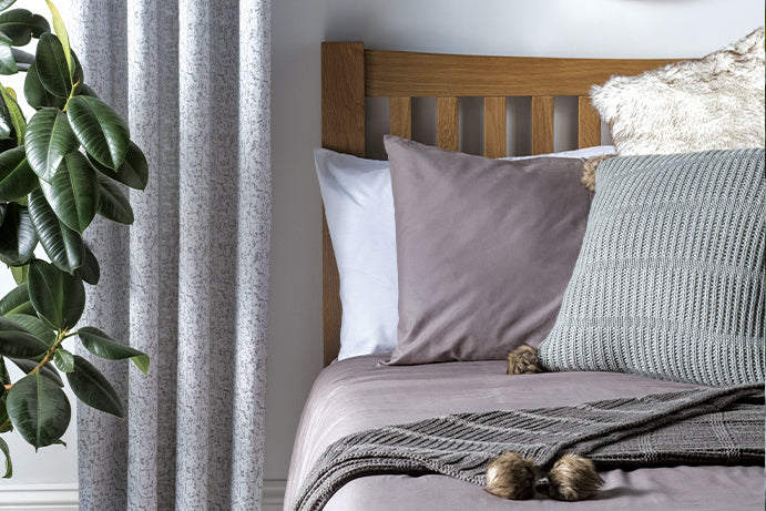 Close up of mixed grey bedding dressed with throws and cushions