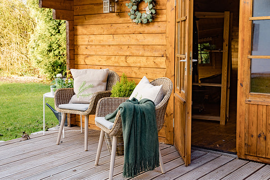 Two relaxing garden armchairs on the porch of a wooden summerhouse with an open door