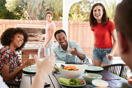 Friends laughing and enjoying dinner under a gazebo in a sunny garden