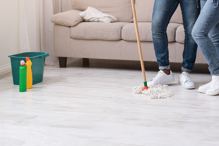 Two individuals cleaning a white floorboard with mops, working together to maintain cleanliness and shine