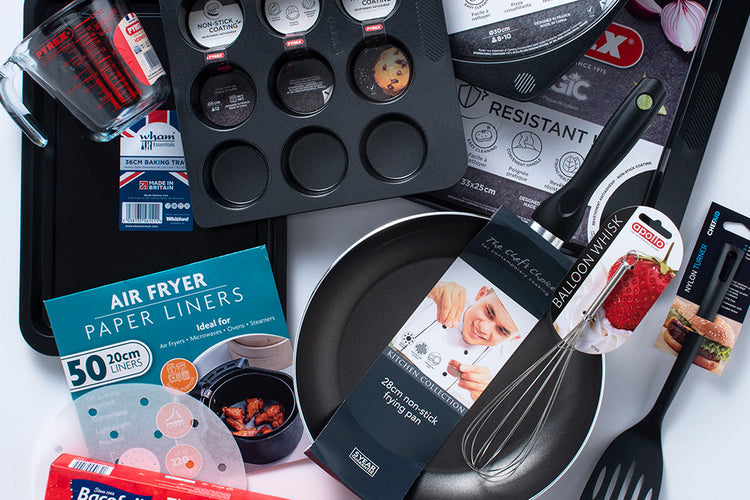 Range of kitchenware such as utensils, muffin trays and frying pans laid out on a white table