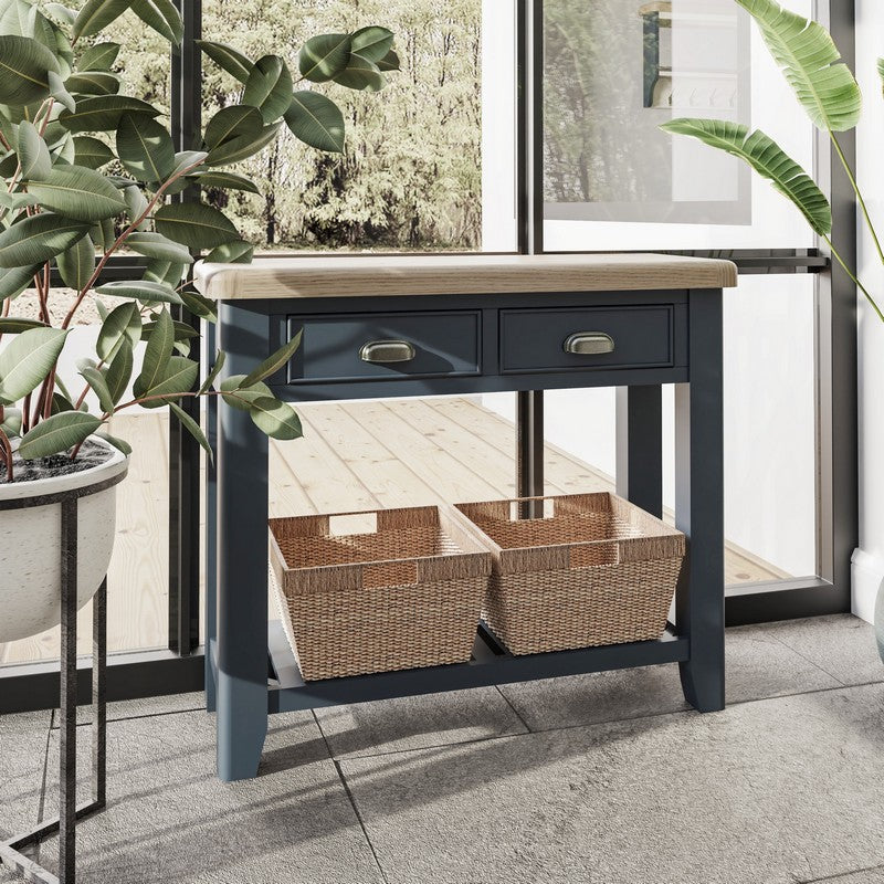 A dark console table featuring two woven baskets and two drawers next to green foliage