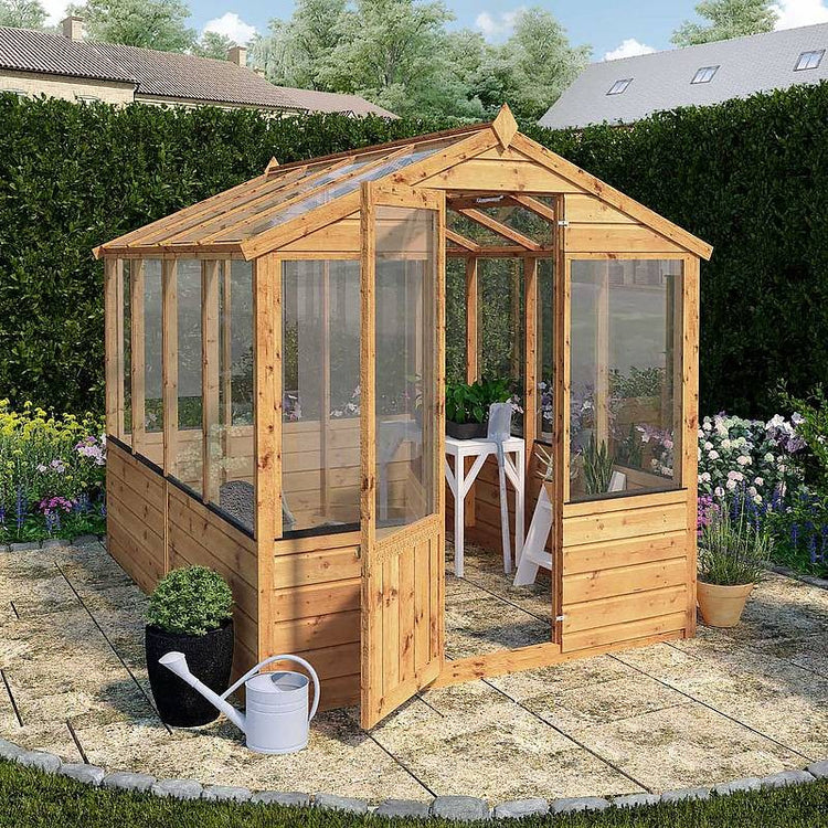 A wooden greenhouse situated on a patio, filled with an abundance of green plants thriving inside