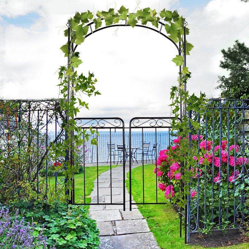 A decorative black arch with climbing green leaves, surrounded by blooming plants