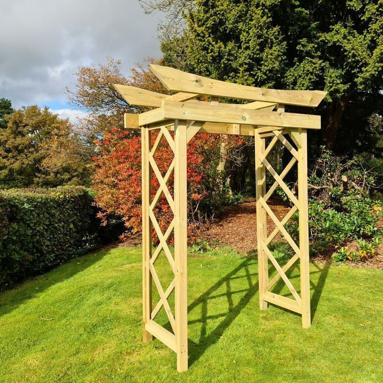 A wooden garden archway standing on grass surrounded by bushes