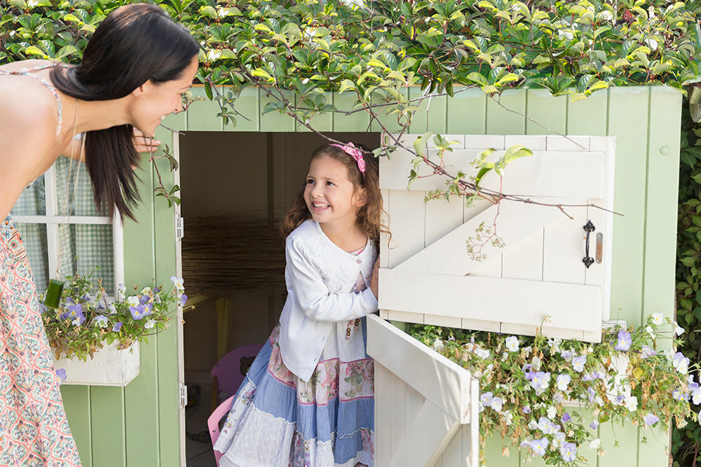 Young girl and adult lady, playing inside a green wooden playhouse 