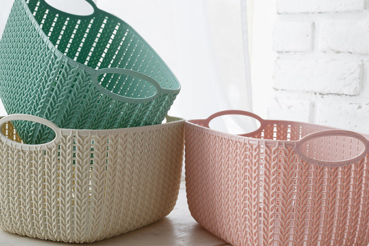 Three storage baskets coloured green, white and pink, placed on the floor