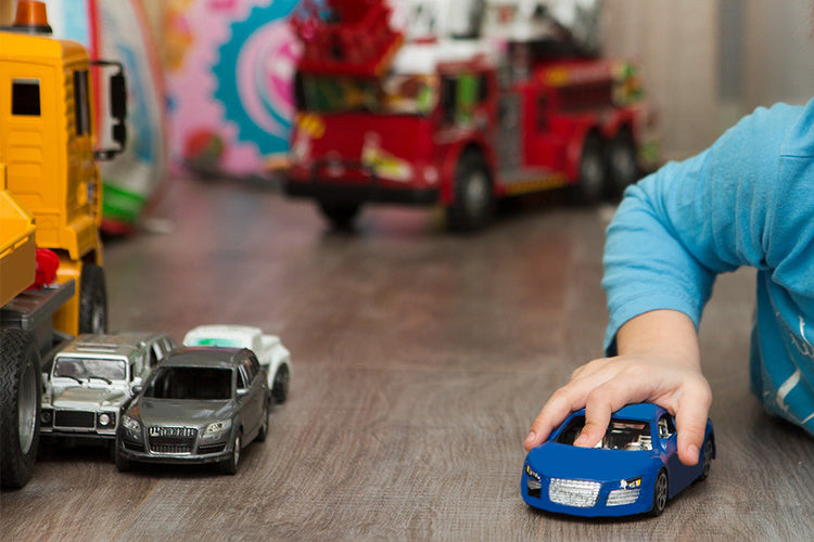 Child playing with a blue toy car an a range of other vehicle related toys